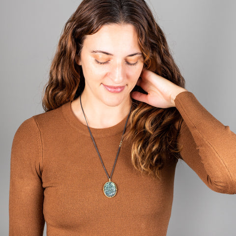 A large labradorite stone is carved with a floral design and set in 18k yellow gold. The large pendant hangs from an oxidized sterling silver chain with three off center blue diamonds set in the chain. 