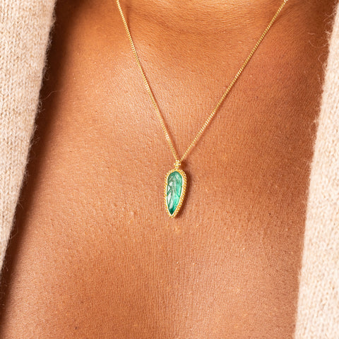 A small emerald is carved into the shape of a leaf and set in an 18k yellow gold chain wrapped bezel. The pendant hangs on a short delicate chain
