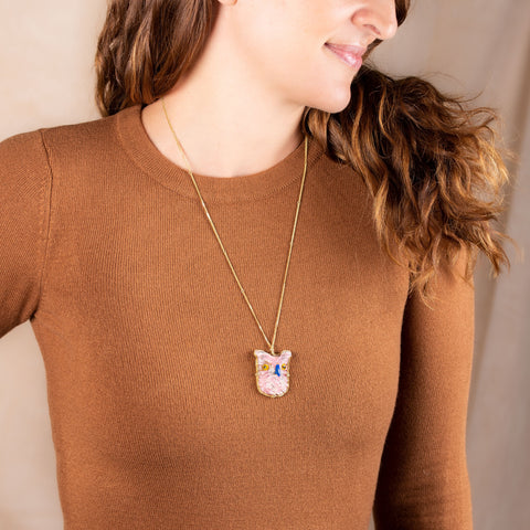 A model wears a pendant made with a light pink rhodochrosite stone carved into an owl and set in an 18k yellow gold bezel on a long delicate chain.