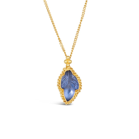A carved leaf shaped tanzanite stone is set in an 18k yellow gold bezel with a braided detail around the edge and hangs from a delicate gold chain.