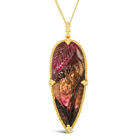 This teardrop shaped floral and leaf carved tourmaline is set in an 18k yellow gold chain wrapped bezel with four beaded prongs. The pendant hangs on a delicate chain.
