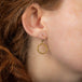 This pair of 18k yellow gold earrings features a small circle hoop crafted in chain to create a stardust-like effect. The circle hangs from a French hook closure.
