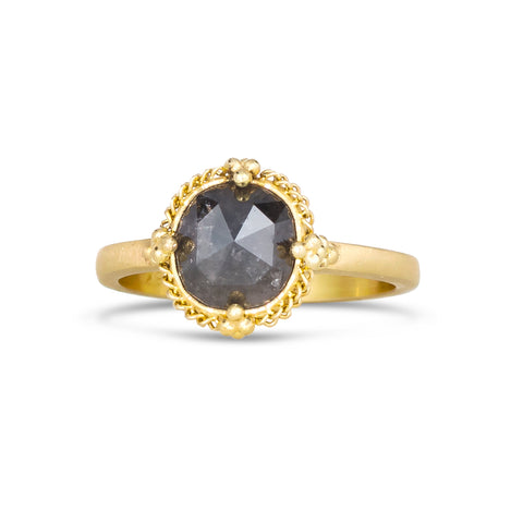 A small circular salt and pepper diamond ring is set in an 18k yellow gold chain wrapped bezel with four beaded prongs. The stone sits on a thin band.