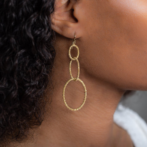 This pair of earrings features three graduated interlocking circles crafted from a woven chain to create a stardust like effect. The earrings hang from French hook closures.