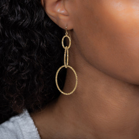 A model wears an earring crafted with three graduated interlocking circles made in 18k yellow gold with a stardust like effect.
