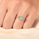 A model wears a small rectangular opal ring set in an 18k yellow gold chain wrapped bezel with four granulated prongs.