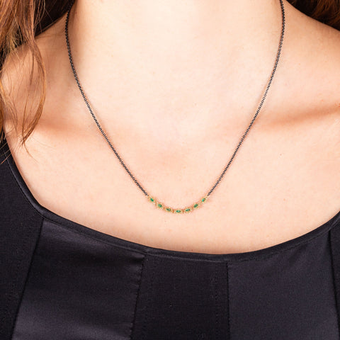 A model wears a short oxidized sterling silver necklace with a row of emeralds set in 18k yellow gold in the center.