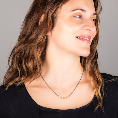 A model wears a short oxidized sterling silver chain necklace with a row of 18k yellow gold wrapped pearls in the center. 