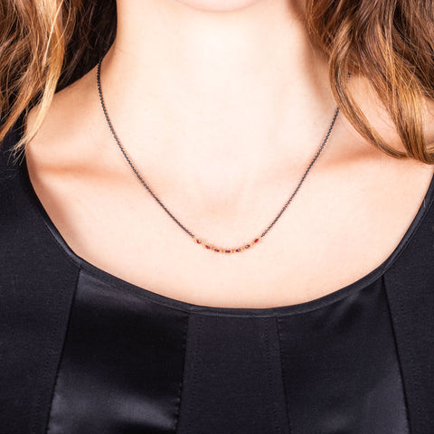 A model wears a short necklace with 18k yellow gold wrapped rubies set in the center of an oxidized sterling silver chain. 