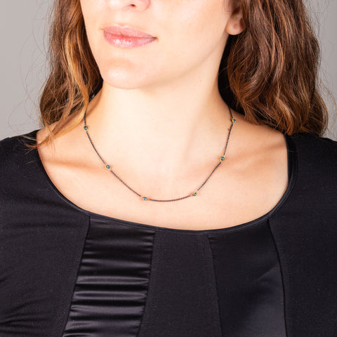 A model wears a short oxidized sterling silver necklace with stations of 18k yellow gold wrapped blue diamonds throughout.