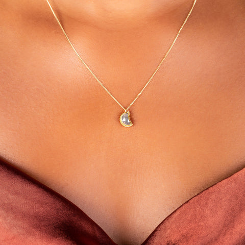 A small charcoal colored diamond cut in the shape of a crescent is set in an 18k yellow gold chain wrapped bezel. The pendant hangs on a delicate chain.