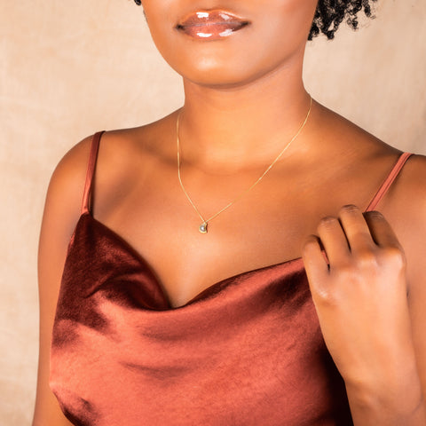 A model wears a small crescent shaped charcoal diamond pendant set in an 18k yellow gold chain wrapped bezel. The pendant hangs on a delicate chain.