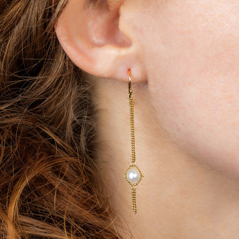 A model wears a long pearl earring suspended in 18k yellow gold chain.