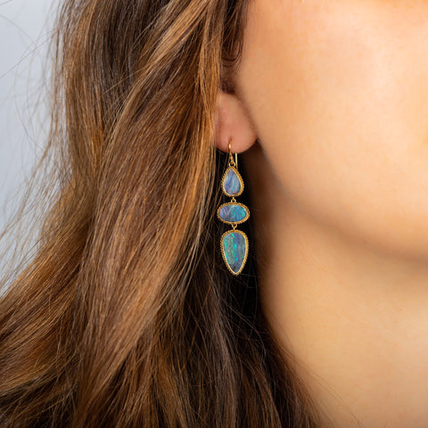This pair of boulder opal earrings feature three stones wrapped in 18k yellow gold chain wrapped bezels. The stones hang from a French hook closure.