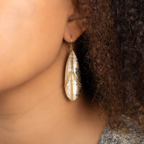 A model wears a large teardrop shaped tan and brown opal earring draped in 18k yellow gold chain and champagne diamonds.