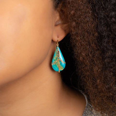 A model wears a large teardrop shaped turquoise earring draped in 18k yellow gold chain and champagne diamonds. 