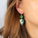 A model wears a large earring that features a rectangular emerald and teardrop shaped chrysoprase. The stones are set in 18k yellow gold chain wrapped bezels and hang from a French hook closure. 