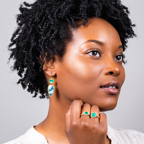 A model wears a large earring that features a rectangular emerald and teardrop shaped chrysoprase. The stones are set in 18k yellow gold chain wrapped bezels and hang from a French hook closure.