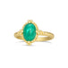 A small oval shaped green emerald is set in an 18k yellow gold chain wrapped bezel with four beaded prongs. The emerald sits on a thin ring band.