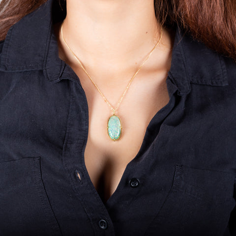 A large oval shaped Ethiopian opal pendant is set in an 18k yellow gold chain wrapped bezel with four beaded prongs. The pendant hangs on a delicate short chain.