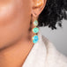 A model wears an Ethiopian opal earring displaying stunning blue hues. Three oval shaped stones are each set in an 18k yellow gold chain wrapped bezel that hang from a French hook.