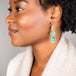A model wears an Ethiopian opal earring displaying stunning blue hues.  Three oval shaped stones are each set in an 18k yellow gold chain wrapped bezel that hang from a French hook.