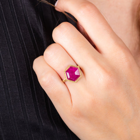 A model wears a large hexagon shaped faceted ruby ring set in 18k yellow gold with a braid embellished bezel.