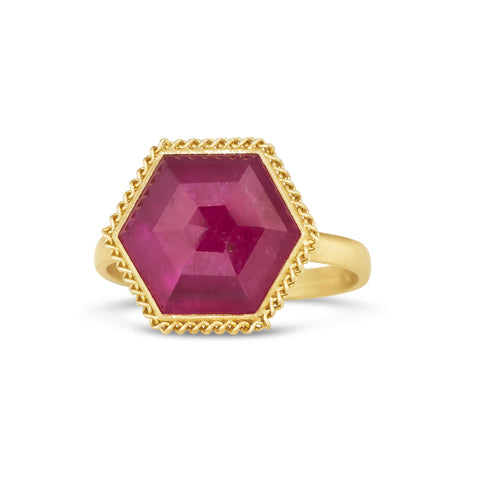 A large hexagon shaped faceted ruby is set in an braid-wrapped 18k yellow gold bezel on a thin ring band.