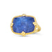 A large faceted rectangular tanzanite stone ring is set in an 18k yellow gold chain wrapped bezel with four beaded prongs. The stone sits on a thin band.