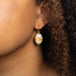 A model wears an oval shaped Mexican opal earring set in an 18k yellow gold chain wrapped bezel with four beaded prongs.