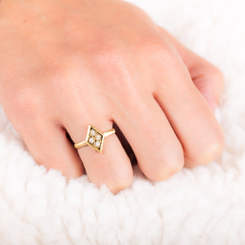 A model wears a diamond shaped ring that is crafted with four small chain wrapped silver diamonds and set in an 18k yellow gold bezel. The ring is set on a thin band.