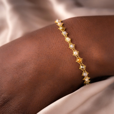 This 18k yellow gold bracelet features multi-colored diamond beads woven throughout a delicate chain.