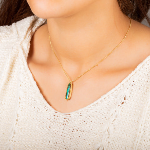 A model wears an elongated opalized wood stone set in an 18k yellow gold chain wrapped bezel. The pendant hangs from a short delicate chain.
