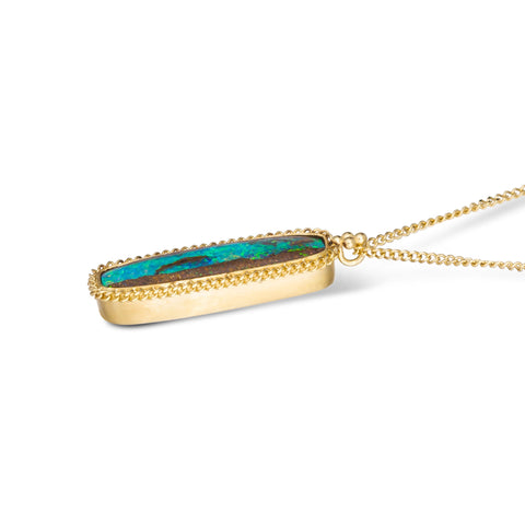 A side view of an elongated opalized wood stone set in an 18k yellow gold chain wrapped bezel. The pendant hangs from a short delicate chain.