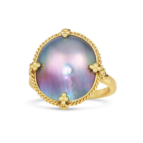 A one-of-a-kind iridescent pearl ring with blue, grey and purple hues is set in a chain wrapped 18k yellow gold bezel with four beaded prongs on a thin gold band. 