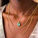 A model wears three layered necklaces, including a large aquamarine pendant, a pearl chain and a champagne diamond chain necklace.