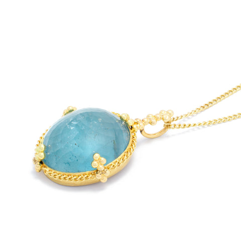 This oval aquamarine pendant is set in an 18k yellow gold chain wrapped bezel with four beaded prongs. The pendant hangs on a delicate chain.