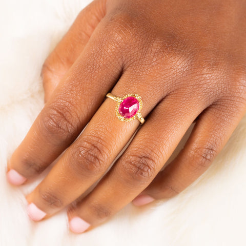 A model wears a small oval shaped faceted ruby ring with an 18k yellow gold bezel that features four granulated prongs.