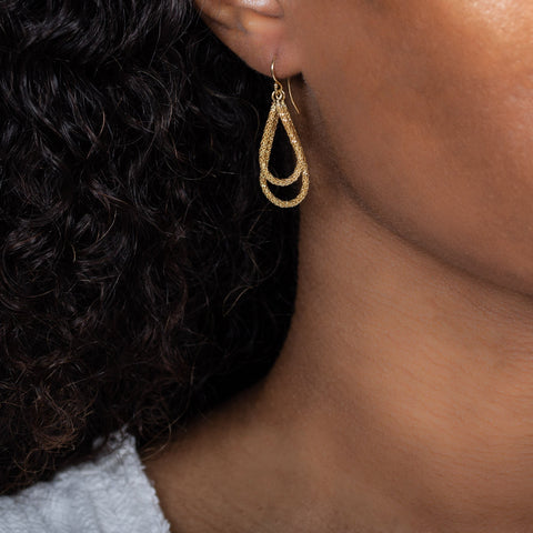 A model wears a large 18k yellow gold interlocking teardrop hoop earring.