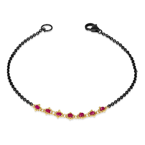 This oxidized sterling silver bracelet features a row of red rubies suspended in 18k yellow gold chain in the center.