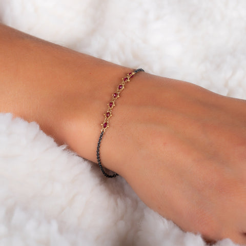 This oxidized sterling silver bracelet features a row of red rubies suspended in 18k yellow gold chain in the center.
