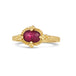 A small oval shaped faceted ruby is set in 18k yellow gold with a braided bezel and four granulated prongs on a thin ring band.