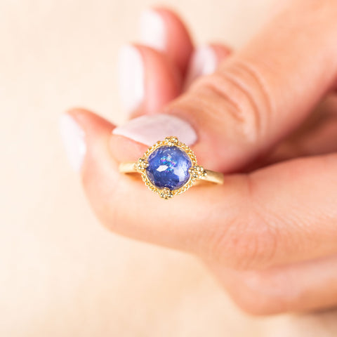 A model holds a faceted round tanzanite stone ring set in 18k yellow gold with four granulated prongs.