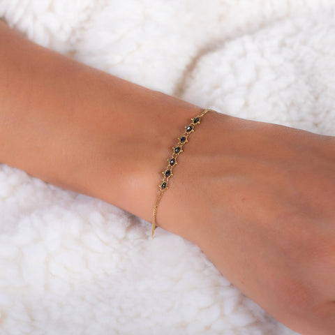 This delicate 18k yellow gold chain bracelet features a row of woven black diamonds in the center and closes with a lobster clasp.