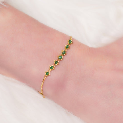 This delicate 18k yellow gold chain bracelet features a row of woven green emeralds in the center and closes with a lobster clasp.