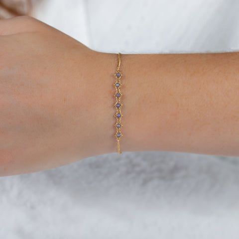 This delicate 18k yellow gold chain bracelet features a row of woven tanzanites in the center and closes with a lobster clasp.