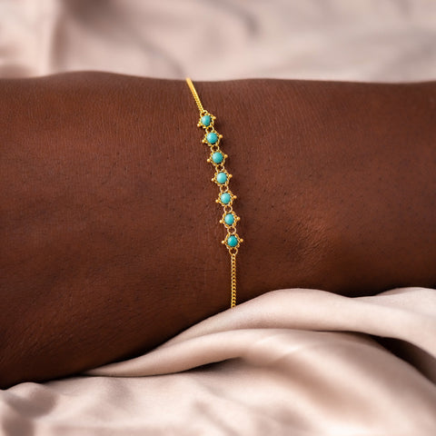 This delicate 18k yellow gold chain bracelet features a row of woven turquoise stones in the center and closes with a lobster clasp.