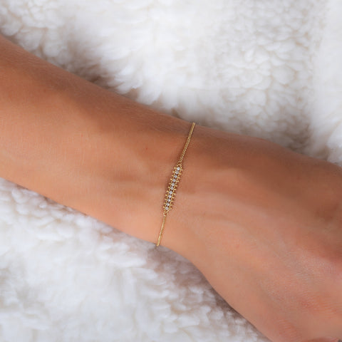 This delicate 18k yellow gold chain bracelet features a row of woven silver diamonds in the center and closes with a lobster clasp.