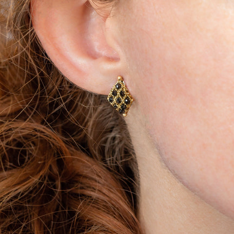 A model wears an earring crafted in 18k yellow gold chain and black diamonds that are woven into a diamond lattice pattern and fastened with a post closure.