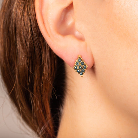 A model wears an earring crafted in 18k yellow gold chain and blue diamonds that are woven into a diamond lattice pattern and fastened with a post closure.